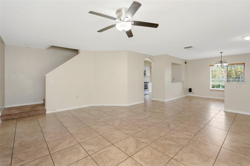 An open-concept living area features beige tile flooring, a ceiling fan, and carpeted stairs — 7361 E BANK DRIVE, TAMPA, FL