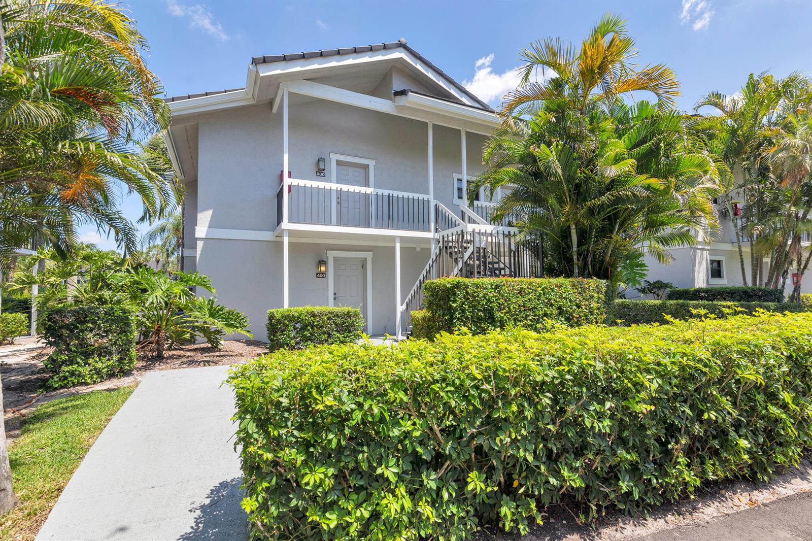 A two-story apartment building features a ground-level entrance, an upper balcony, and lush landscaping — 11863 Wimbledon Circle, Wellington FL 33414, WELLINGTON, FL