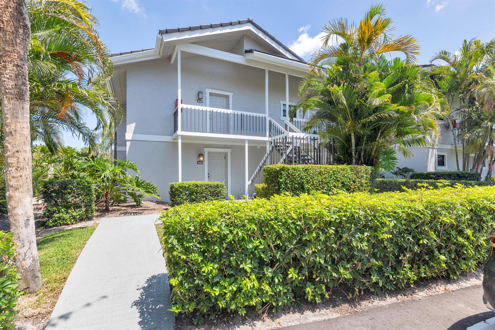 A two-story apartment building with gray siding, a concrete walkway, and surrounding tropical landscaping — 11863 Wimbledon Circle, Wellington FL 33414, WELLINGTON, FL