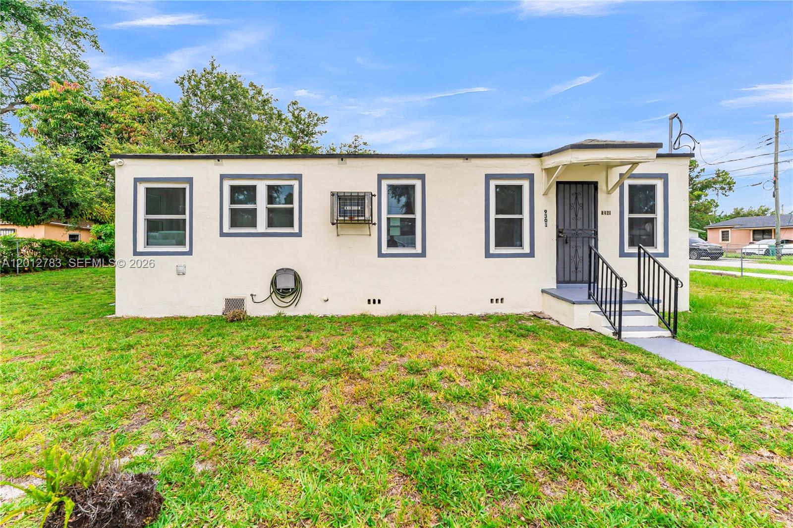 A single-story, light-colored house with a front entrance, several windows, and a grassy yard — 9301 NW 20th Ave, Miami FL 33147, MIAMI, FL