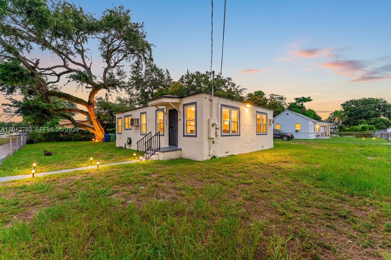 A small, light-colored single-story house sits on a grassy lot with a large tree — 9301 NW 20th Ave, Miami FL 33147, MIAMI, FL