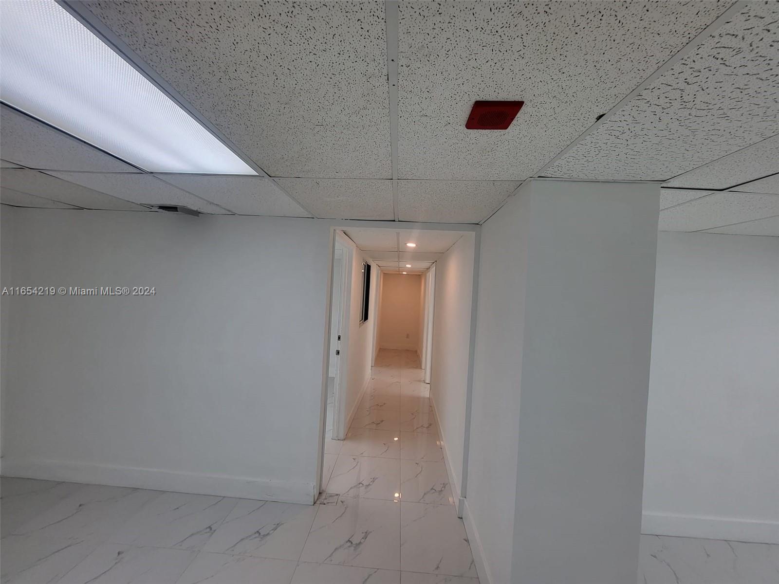 A hallway with white marble-patterned tile floors leads from a room with a drop ceiling — 13499 Biscayne Blvd, North Miami FL 33181, NORTH MIAMI, FL
