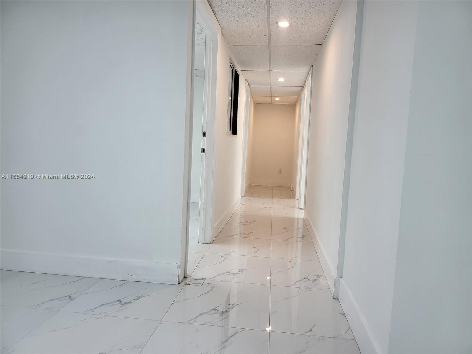 A hallway features white marble-patterned tile flooring, white walls, and a drop ceiling with recessed lighting — 13499 Biscayne Blvd, North Miami FL 33181, NORTH MIAMI, FL