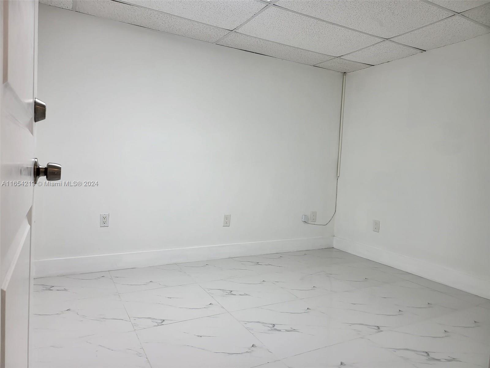 An empty room features white walls, marble-patterned tile flooring, and a drop ceiling — 13499 Biscayne Blvd, North Miami FL 33181, NORTH MIAMI, FL