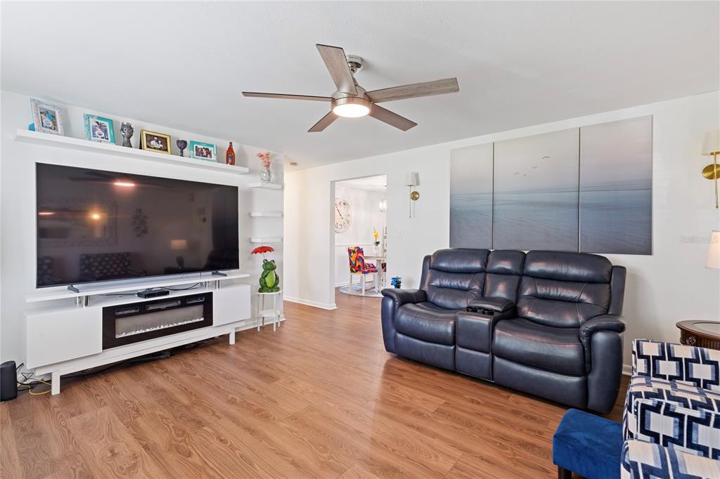 A living room features a large television, a dark leather sofa, and wood-look flooring — 5906 CYPRESS STREET, ZEPHYRHILLS, FL