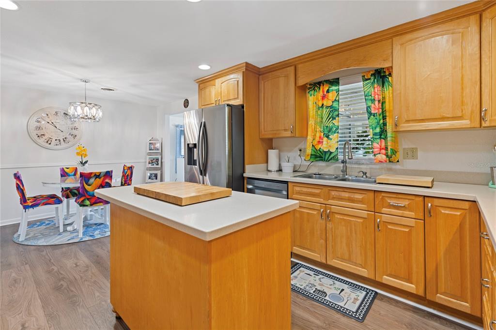 A kitchen with wood cabinets, a central island, and a dining area with colorful chairs — 5906 CYPRESS STREET, ZEPHYRHILLS, FL