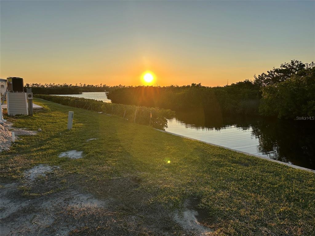 A grassy yard overlooks a canal and dense vegetation at sunset — 732 BLACKBURN BOULEVARD, NORTH PORT, FL