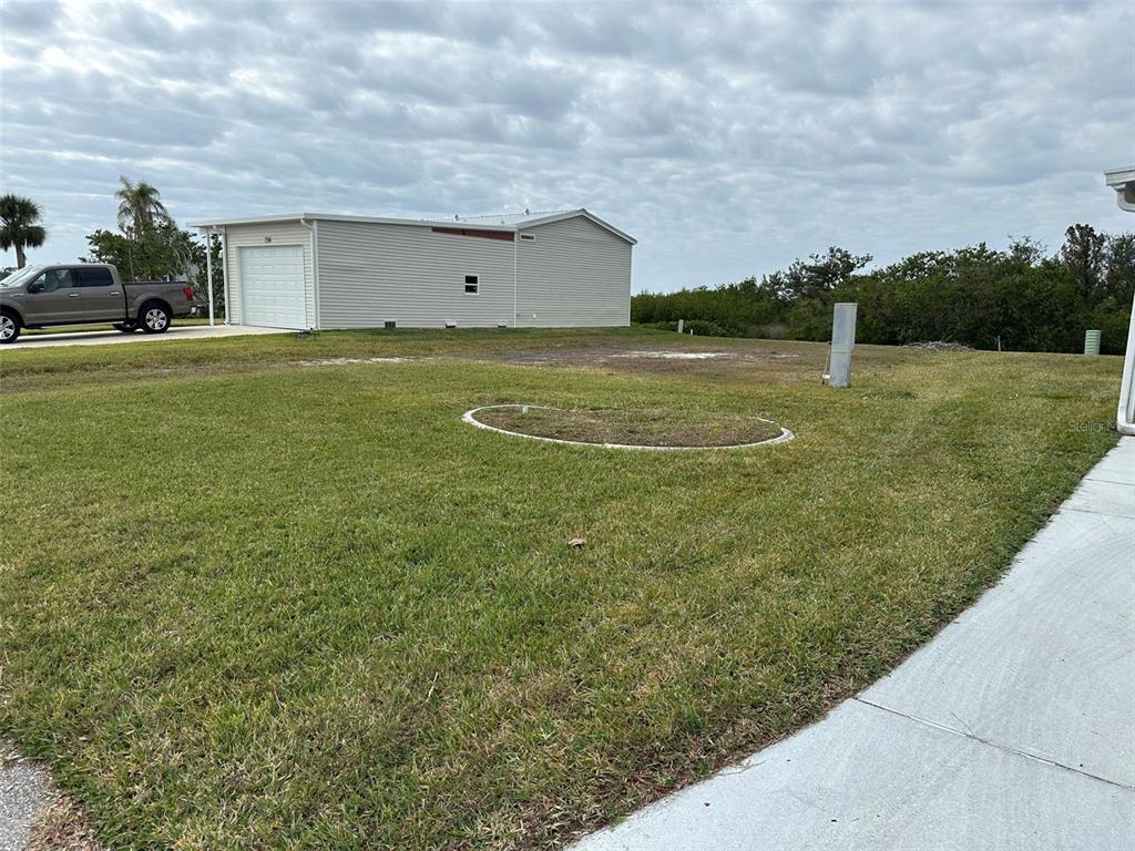 A grassy yard features a circular garden bed and a detached garage in the background — 732 BLACKBURN BOULEVARD, NORTH PORT, FL