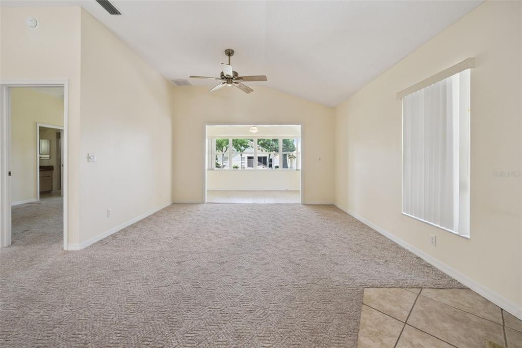 A carpeted living room with a vaulted ceiling, ceiling fan, and a view into a sunroom — 5503 LAVER STREET, LEESBURG, FL