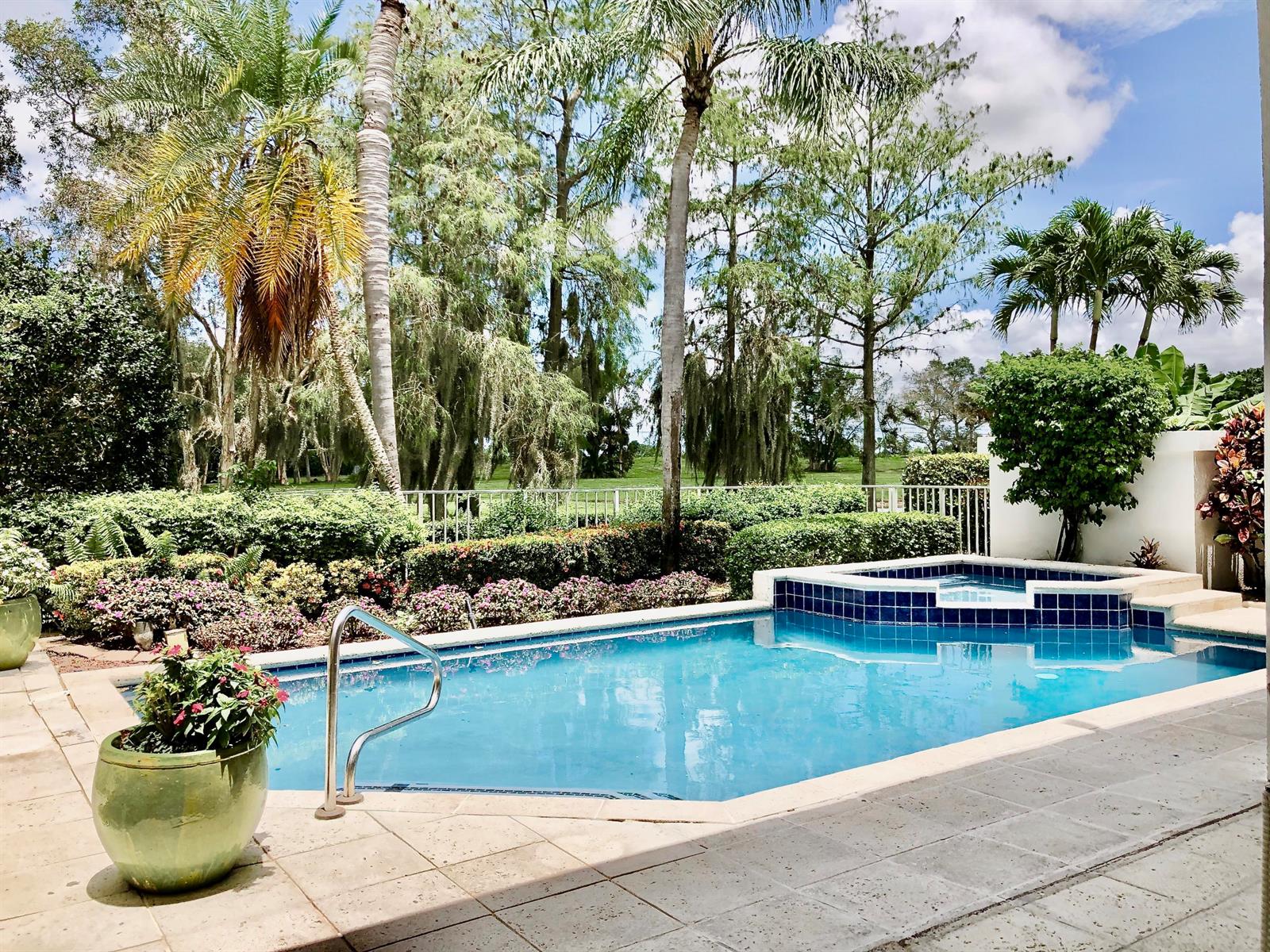 A backyard swimming pool and attached spa are surrounded by lush landscaping and tall trees — 2313 Golf Brook Drive, Wellington FL 33414, WELLINGTON, FL