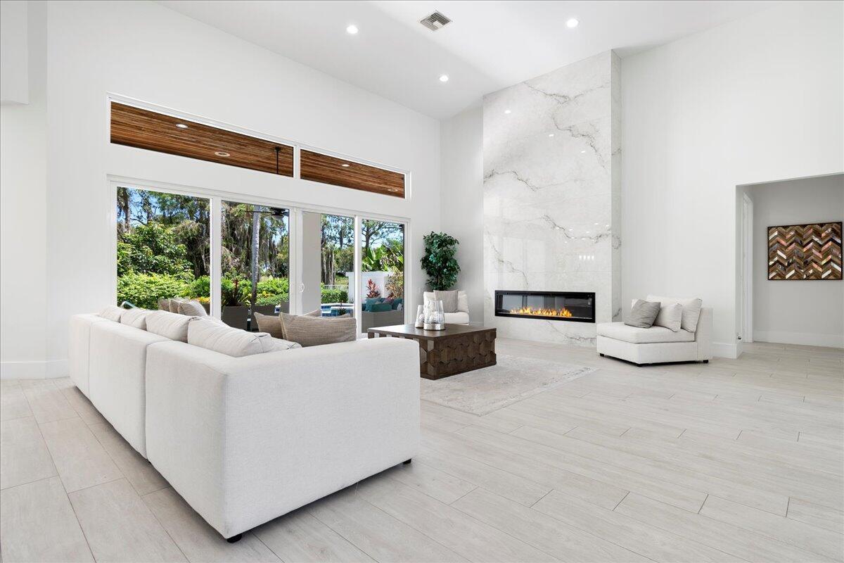 A spacious living room features a white marble fireplace, light tile floors, and large windows — 2313 Golf Brook Drive, Wellington FL 33414, WELLINGTON, FL