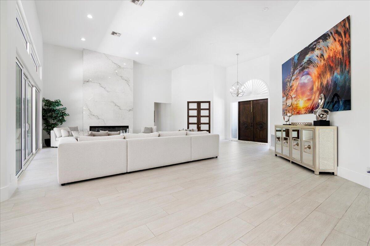 A spacious living room features light wood-look flooring, a large white sectional, and marble fireplace — 2313 Golf Brook Drive, Wellington FL 33414, WELLINGTON, FL