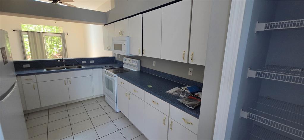 A kitchen features white cabinets, blue countertops, white appliances, and an adjacent open pantry — 12519 HOLLYBROOK LANE, HUDSON, FL