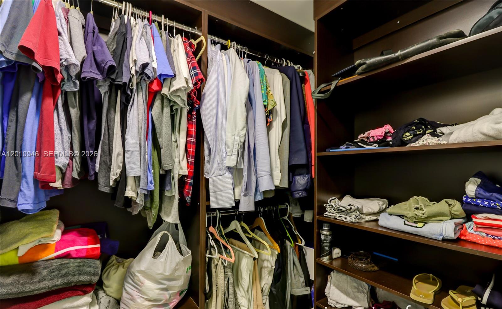 A walk-in closet features dark wood shelving and hanging rods filled with various clothing items — 92 SW 3rd St # 2410, Miami FL 33130, MIAMI, FL