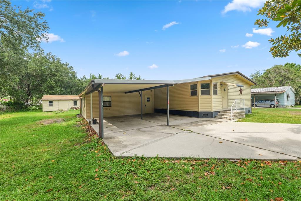 A yellow mobile home features a large attached carport and a concrete driveway — 3159 HONEOYE TRAIL UNIT 42, LAKELAND, FL