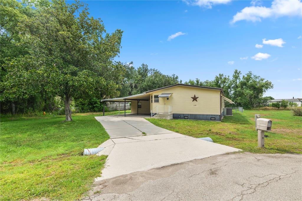 A yellow single-story house with a carport and a concrete driveway sits on a lawn — 3159 HONEOYE TRAIL UNIT 42, LAKELAND, FL