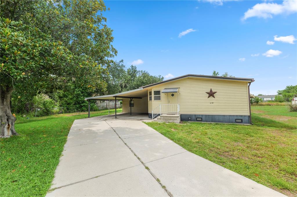 A single-story yellow house with a carport and a large star decoration on the siding — 3159 HONEOYE TRAIL UNIT 42, LAKELAND, FL