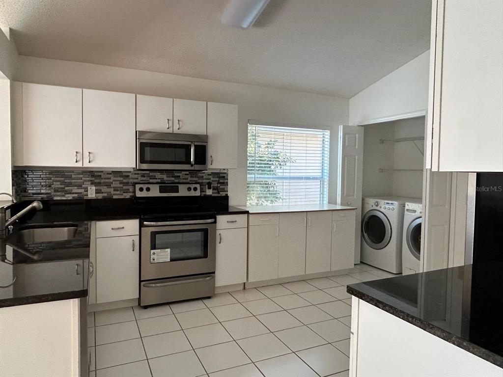 A kitchen with white cabinets, stainless steel appliances, dark countertops, and a laundry closet — 683 RANDON TERRACE, LAKE MARY, FL