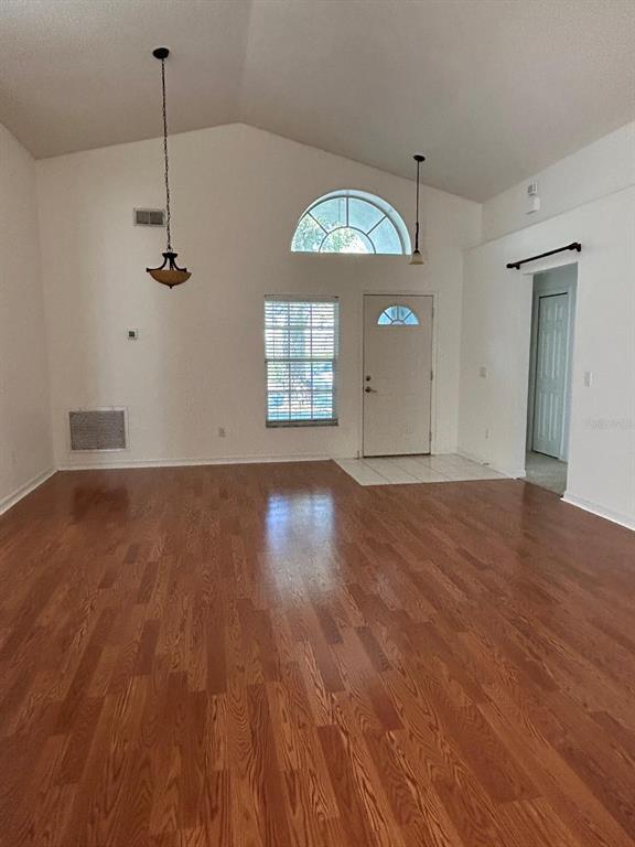 A living room with vaulted ceilings, wood-look flooring, a front door, and two pendant lights — 683 RANDON TERRACE, LAKE MARY, FL