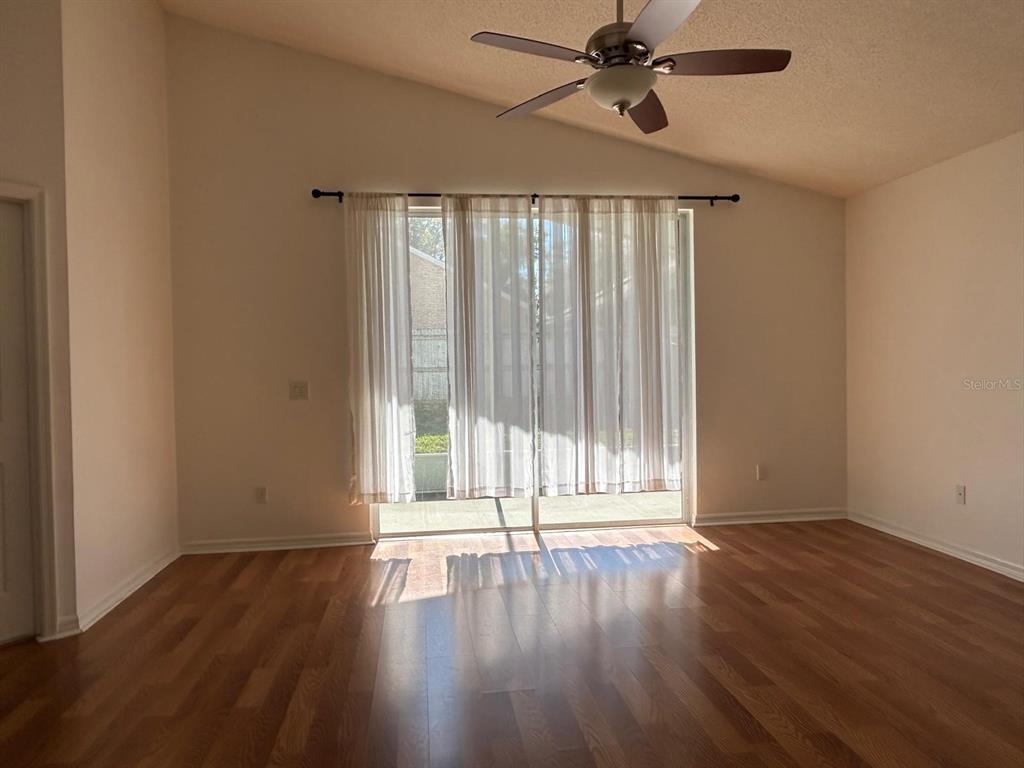 A living room with wood-look flooring, a vaulted ceiling, a ceiling fan, and sliding glass doors — 683 RANDON TERRACE, LAKE MARY, FL