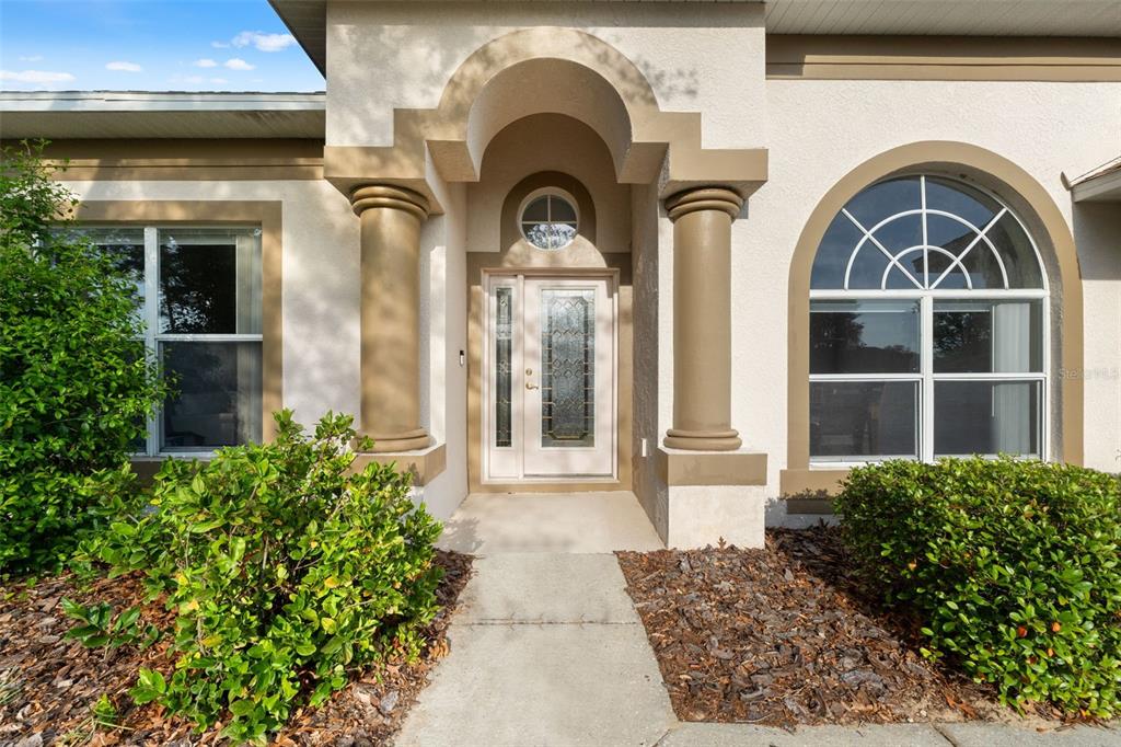 The front entrance of a house features a glass-paneled door, two columns, and arched windows — 5683 BRACKENWOOD DRIVE, SPRING HILL, FL