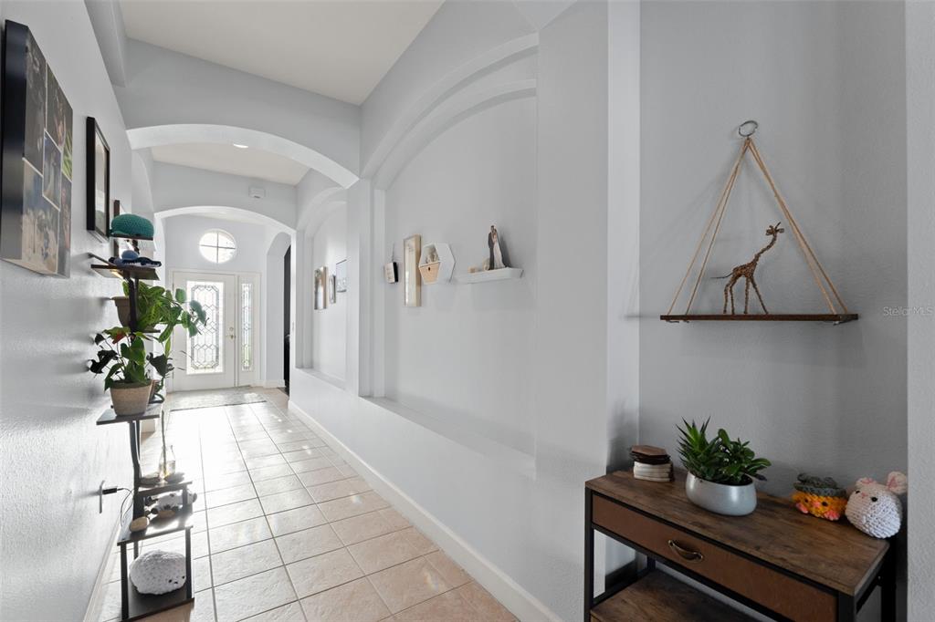 A bright entryway features tiled floors, arched architectural details, and a wall-mounted decorative shelf — 5683 BRACKENWOOD DRIVE, SPRING HILL, FL