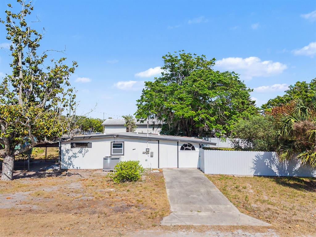 A single-story house with a concrete driveway, white siding, and a large tree in front — 7708 MARYLAND AVENUE, HUDSON, FL