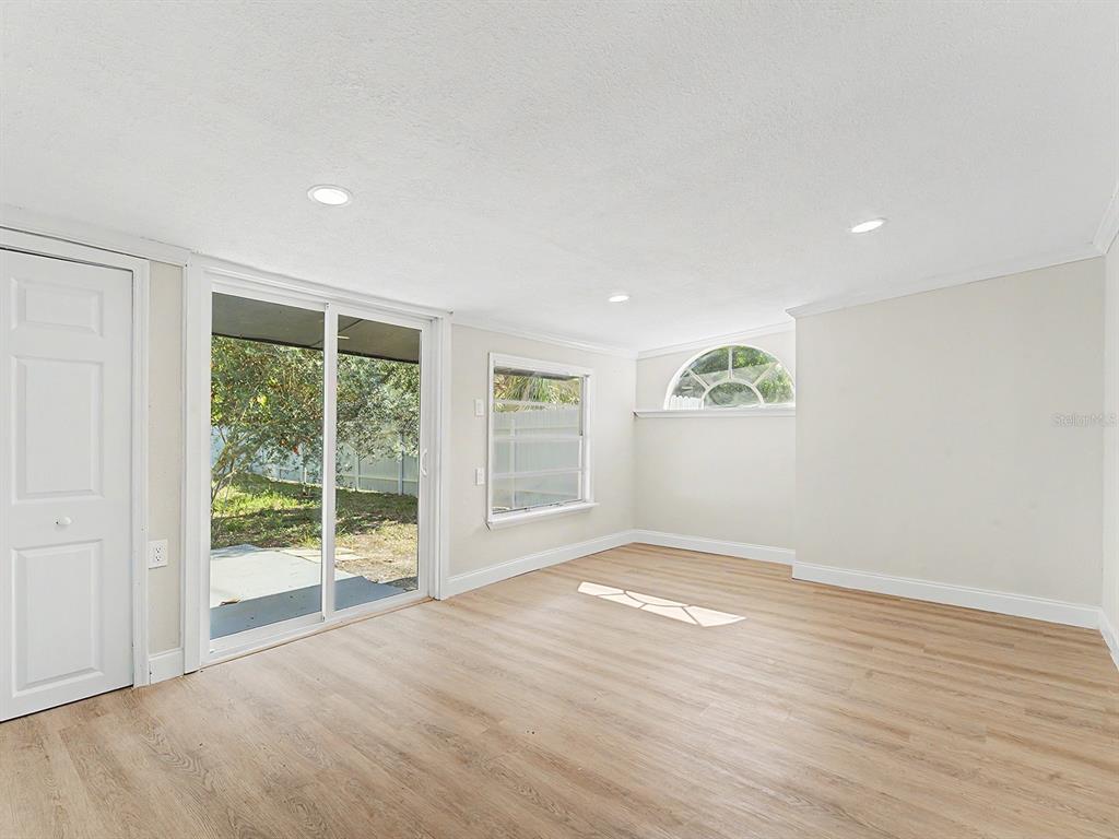 A bright room features light wood-look flooring, recessed lighting, a sliding glass door, and windows — 7708 MARYLAND AVENUE, HUDSON, FL