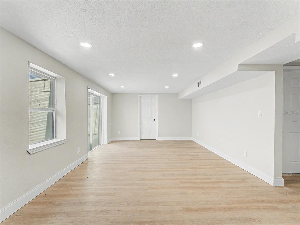 A bright room with light wood-look flooring, recessed lighting, a window, and a sliding door — 7708 MARYLAND AVENUE, HUDSON, FL