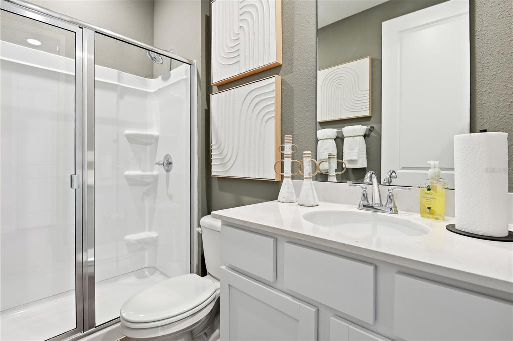 A bathroom features a glass-enclosed shower, a white vanity with a sink, and wall art — 2530 29TH LANE E, PALMETTO, FL