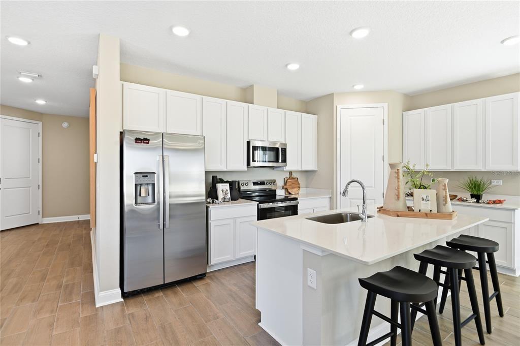 A modern kitchen features white cabinets, stainless steel appliances, a quartz island, and wood-look tile — 2530 29TH LANE E, PALMETTO, FL