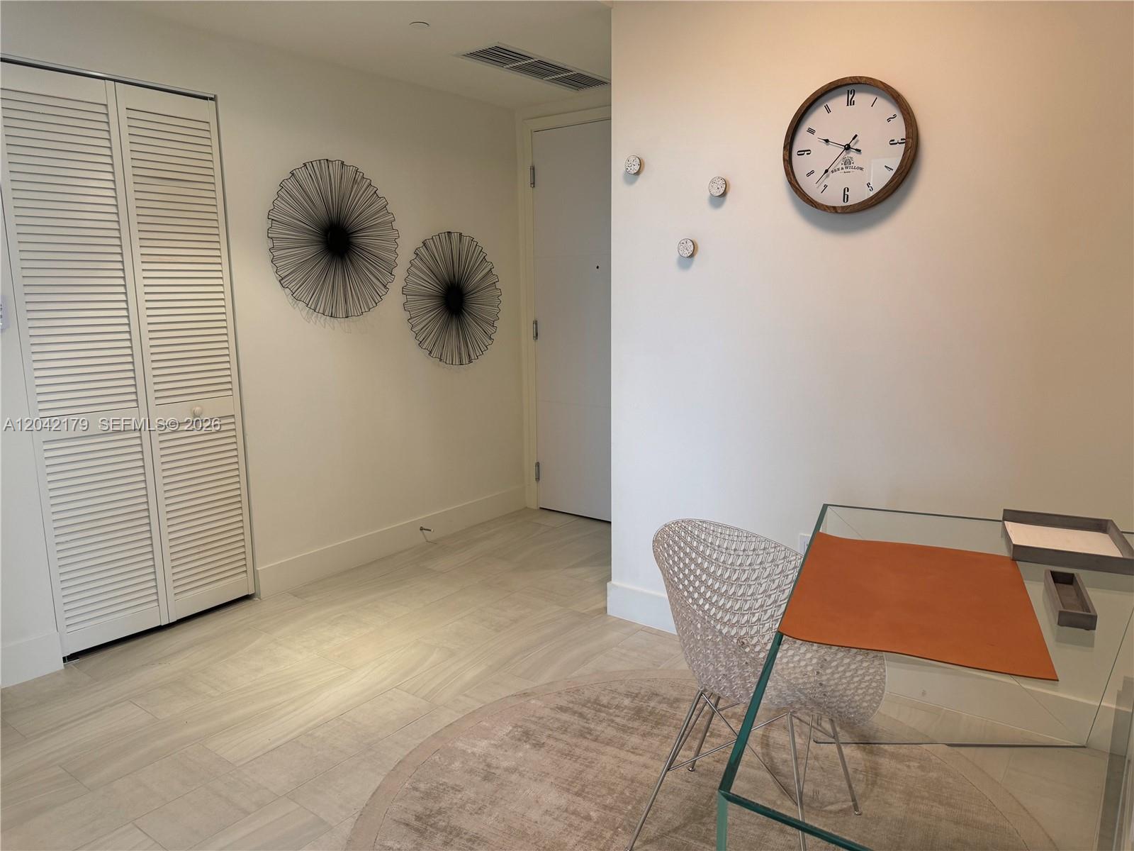 A room features a glass desk, a white chair, wall decor, and a wall clock — 2000 Metropica Way # 903, Sunrise FL 33323, SUNRISE, FL