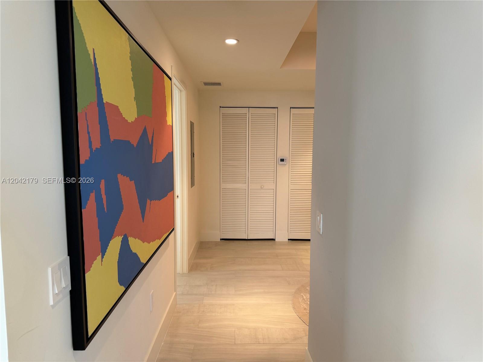 A hallway features light wood-look tile flooring, white louvered closet doors, and a large abstract painting — 2000 Metropica Way # 903, Sunrise FL 33323, SUNRISE, FL