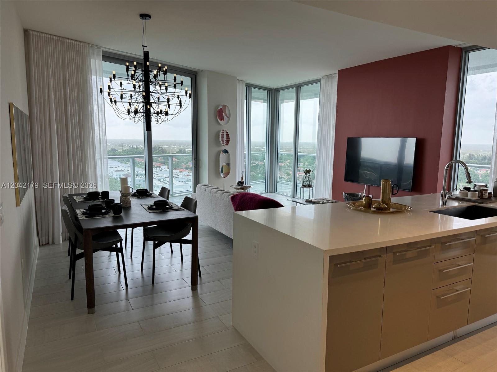 An open-concept living and dining area features floor-to-ceiling windows, a modern chandelier, and kitchen island — 2000 Metropica Way # 903, Sunrise FL 33323, SUNRISE, FL