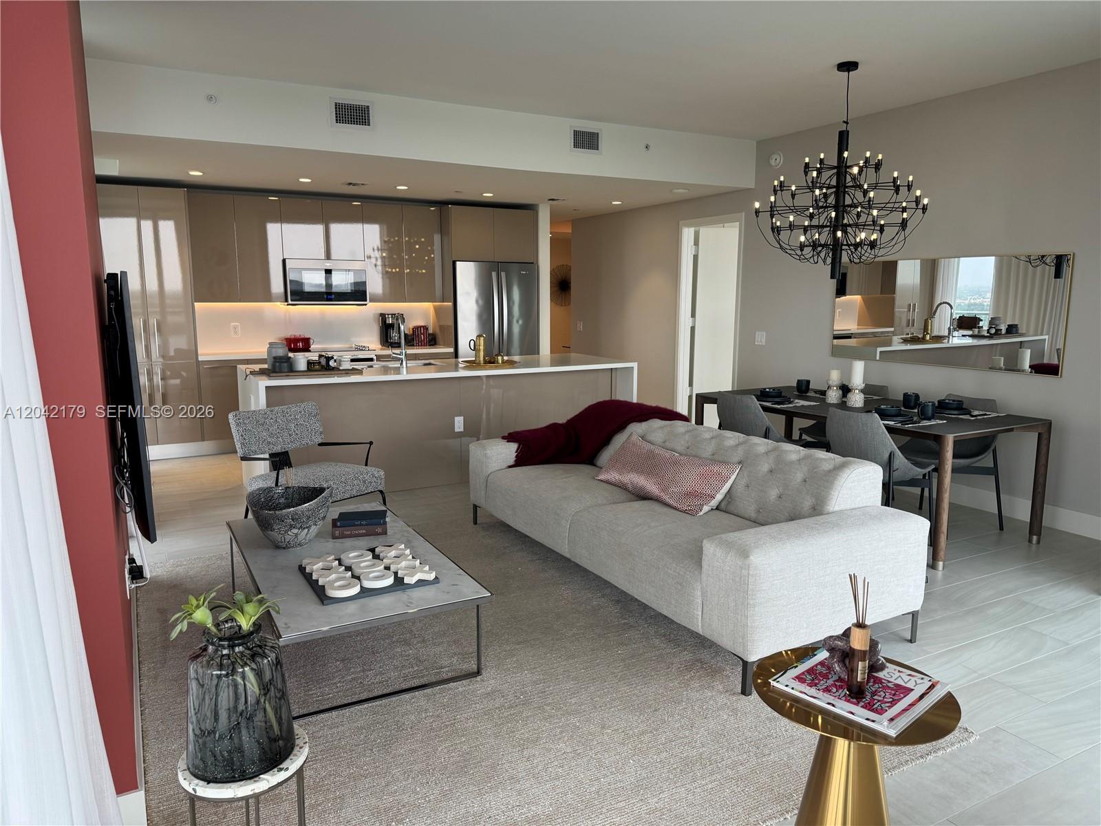 An open-concept living and dining area features a modern kitchen with high-gloss cabinetry — 2000 Metropica Way # 903, Sunrise FL 33323, SUNRISE, FL