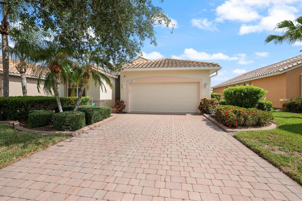 A single-story house with a beige stucco exterior, a tiled roof, and a paved driveway — 4211 64TH AVENUE E, SARASOTA, FL