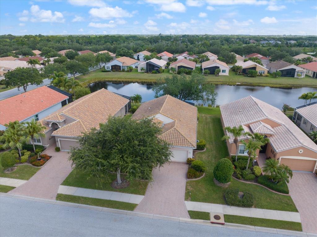 An aerial view shows three suburban houses with tile roofs situated along a small lake — 4211 64TH AVENUE E, SARASOTA, FL