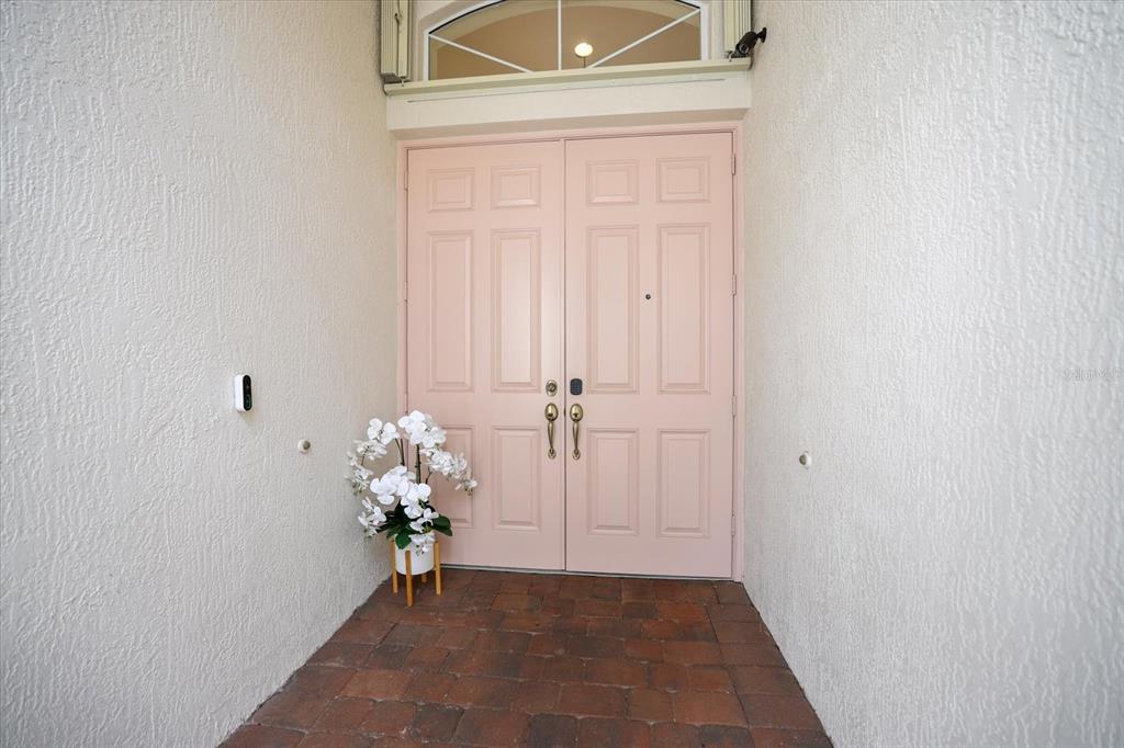 A pink double front door with a white orchid plant sits on a brick porch — 4211 64TH AVENUE E, SARASOTA, FL