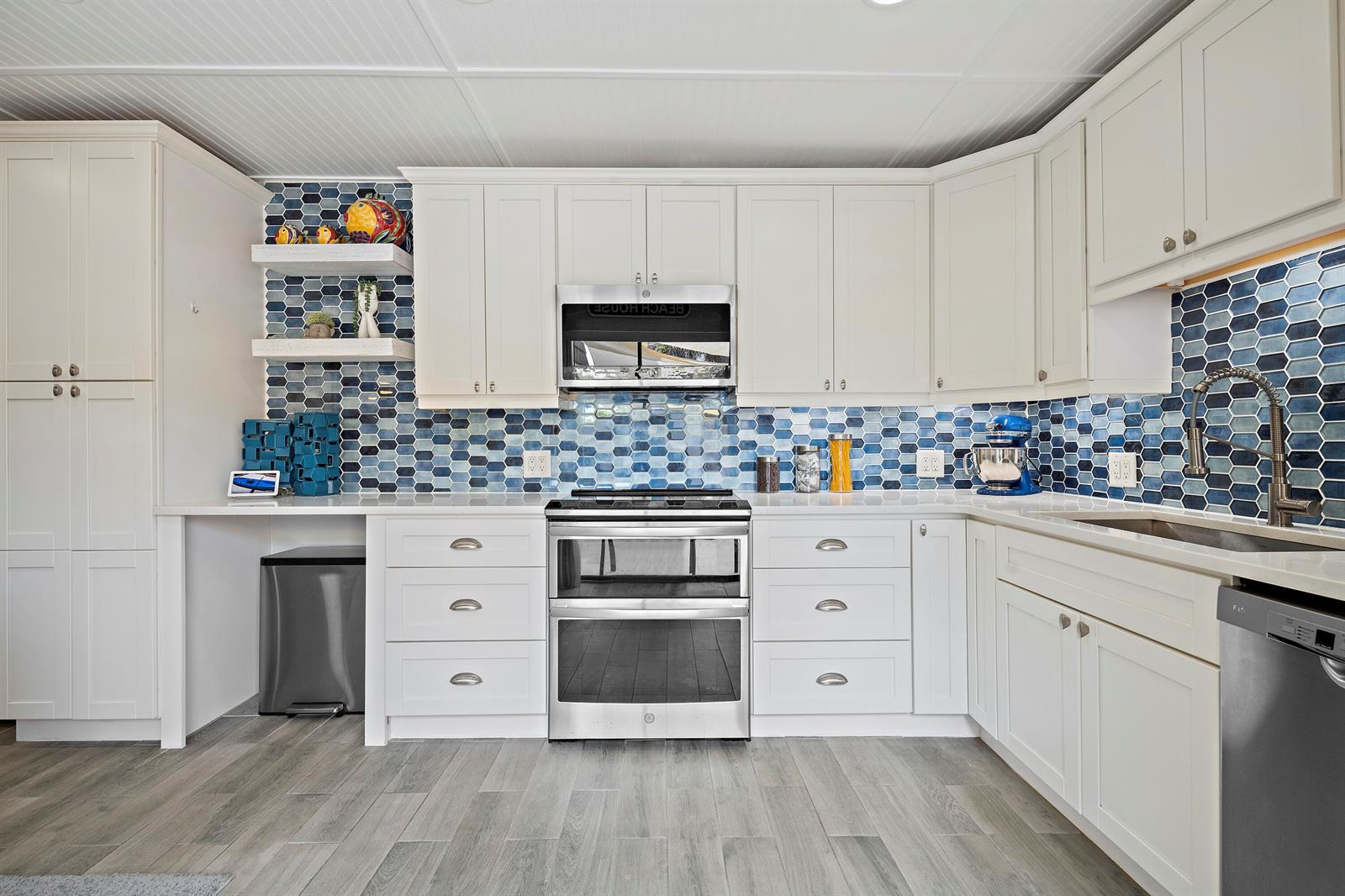 A kitchen features white cabinetry, stainless steel appliances, and a blue hexagonal tile backsplash — 6163 SE Riverboat Drive # 1018, Stuart FL 34997, STUART, FL