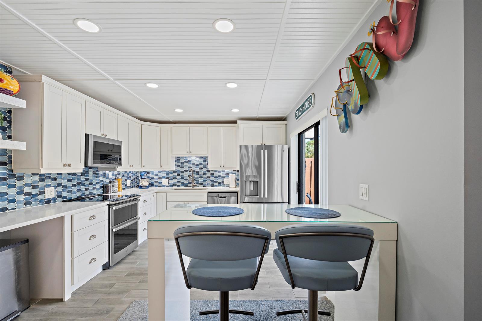 A kitchen features white cabinets, blue hexagonal backsplash tiles, stainless steel appliances, and a dining table — 6163 SE Riverboat Drive # 1018, Stuart FL 34997, STUART, FL