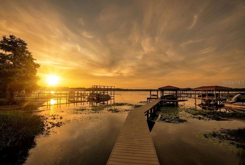 A wooden dock extends into a lake at sunset with boat slips and surrounding trees — 2503 BUTLER BAY DRIVE N, WINDERMERE, FL