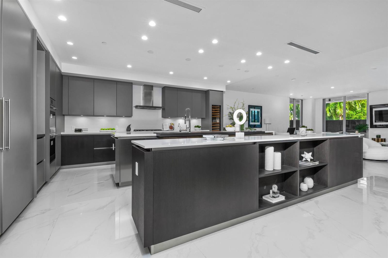 A modern kitchen features dark cabinetry, white marble floors, and a large central island — BOCA RATON, FL