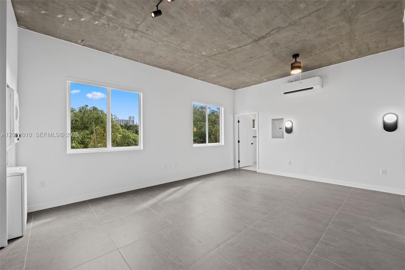An unfurnished room features a raw concrete ceiling, white walls, and large gray floor tiles — 315 NW 32 ST # 307, Miami FL 33127, MIAMI, FL