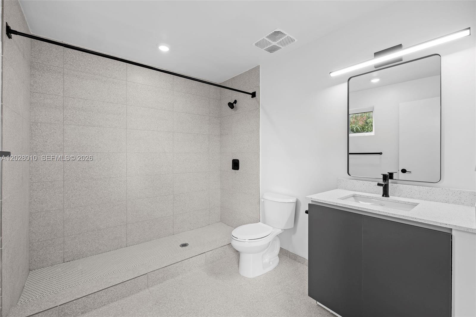 A modern bathroom features a walk-in tiled shower, a white toilet, and a gray vanity — 315 NW 32 ST # 307, Miami FL 33127, MIAMI, FL