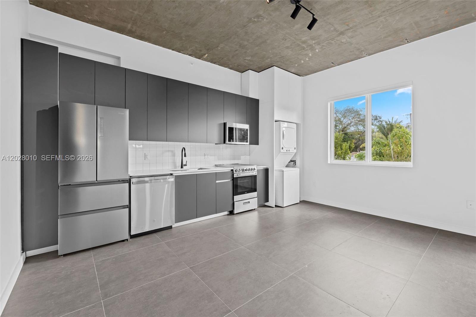 A modern kitchen features dark gray cabinetry, stainless steel appliances, and an exposed concrete ceiling — 315 NW 32 ST # 307, Miami FL 33127, MIAMI, FL