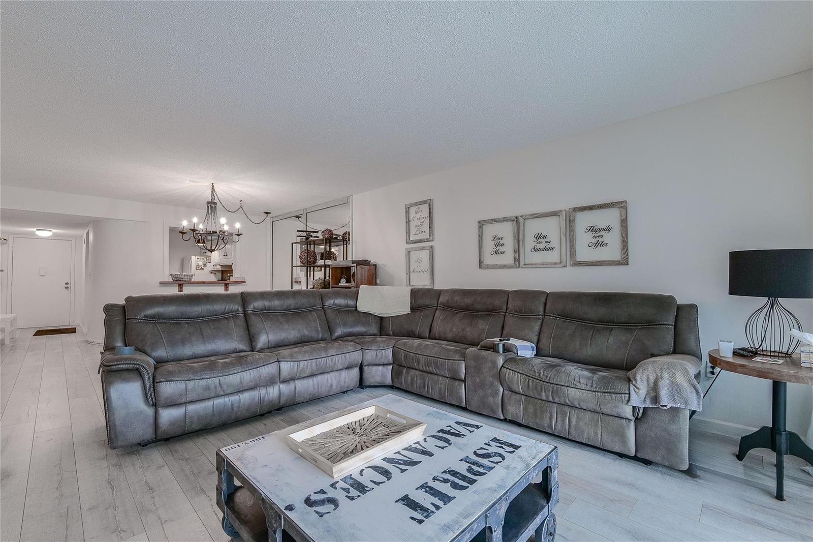 A living room features a large grey sectional sofa, a rustic coffee table, and wall art — 3920 Inverrary Boulevard # C, Lauderhill FL 33319, LAUDERHILL, FL