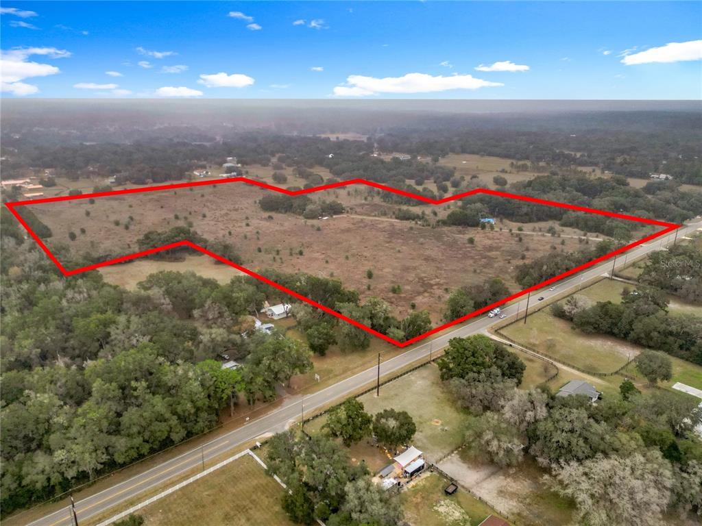 An aerial view shows a large, open, grassy lot outlined in red along a road — 12521 SW HIGHWAY 484, DUNNELLON, FL