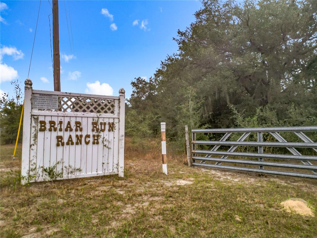A white sign reading Briar Run Ranch stands beside a metal gate and trees — 12521 SW HIGHWAY 484, DUNNELLON, FL