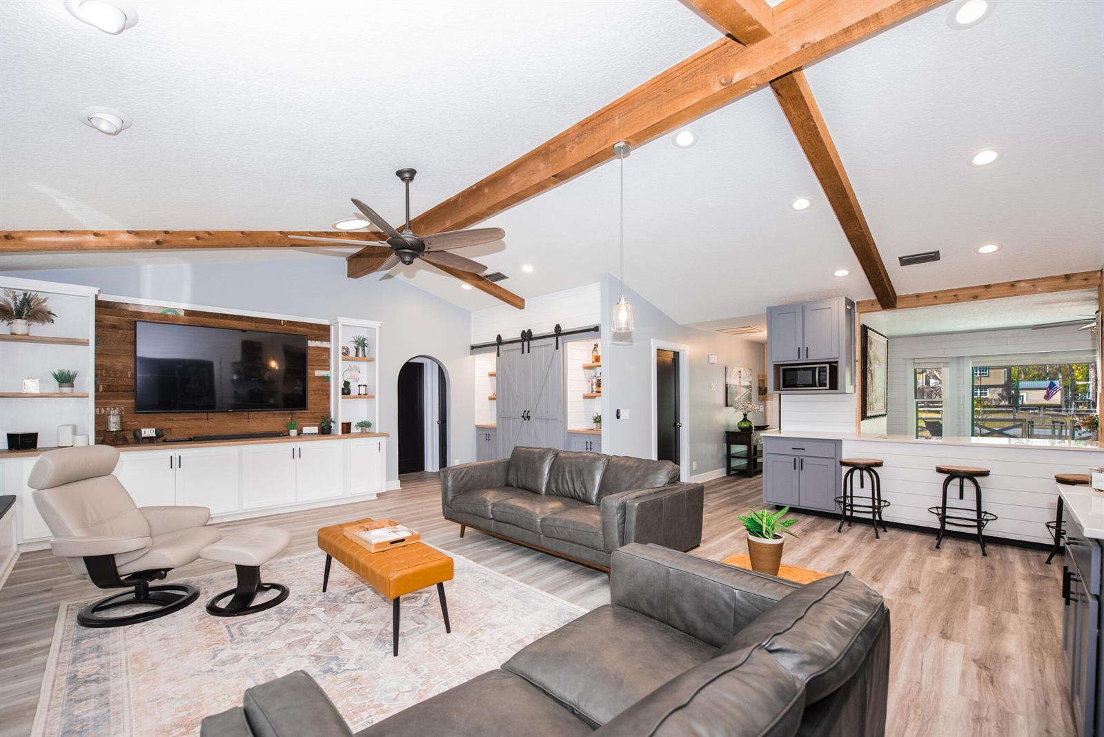 A living room with vaulted ceilings, exposed wooden beams, gray sofas, and an open kitchen — 12970 179th Ct N, Jupiter FL 33478, JUPITER, FL