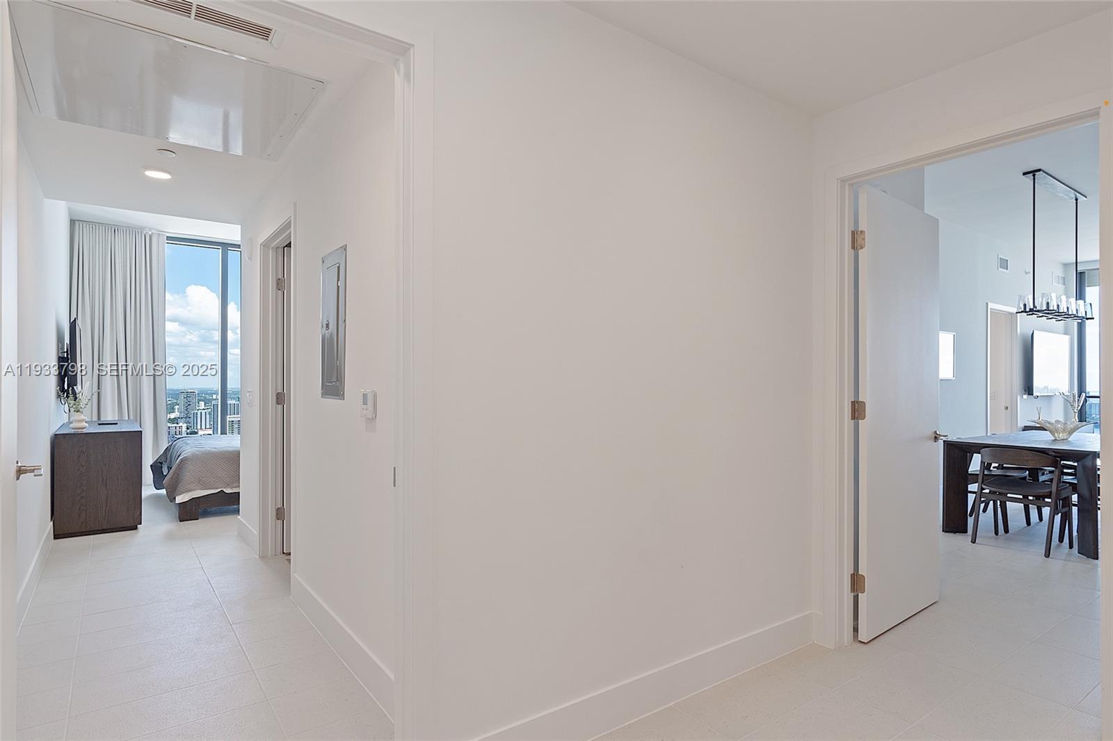 A white hallway connects a bedroom with floor-to-ceiling windows to a dining area — 159 NE 6th St # 5015, Miami FL 33132, MIAMI, FL